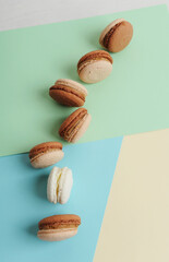 Chocolate and coffee french macarons cookies on colorful pastel background, top view.
