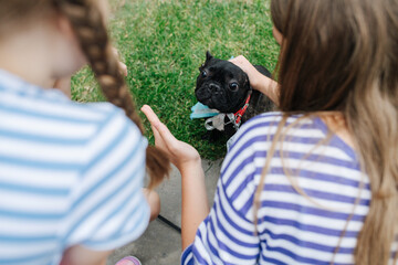 Little girls petting a black pug dog, pulling skin on the head back
