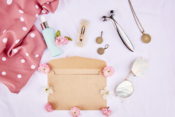 Feminine spring envelope mock up with pink flowers, sunglasses with sky reflection, accessories, massager, cosmetic gift on fabric white background. 8 of March concept