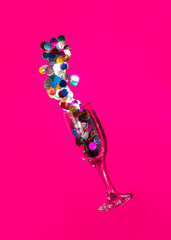 Party drink. Glass full of confetti on pink background. Minimalistic birthday cocktail concept.