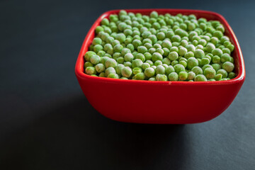 frozen frosty green peas in red ceramic bowl closeup