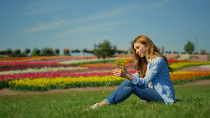 Beautiful girl sitting on grass in summer day. Relaxed girl enjoying wild flower