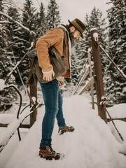 bearded man in a hat with backpack walking on a wooden bridge, snowy winter