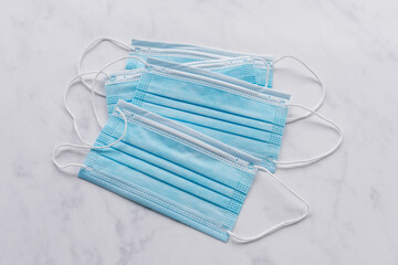 Four single use disposable blue face masks on white marble