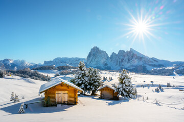 Picturesque landscape with small wooden log cabin on meadow Alpe di Siusi on winter time. Seiser Alm, Dolomites, Italy. Snowy hills with orange larch and Sassolungo and Langkofel mountains group