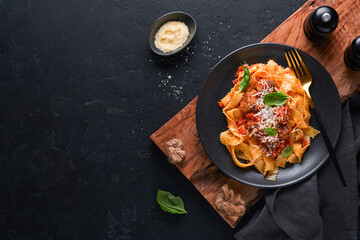 Tagliatelle pasta with meatballs in tomato sauce, basil and parmesan cheese on black stone or concrete background. Traditional Italian dish and cuisine. Top view with copy space.