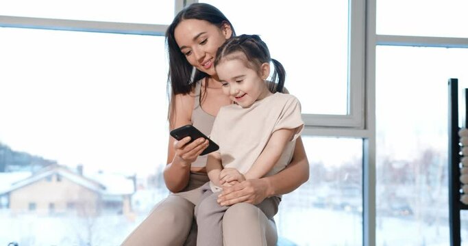 A little girl sits on her mother's lap and looks at the phone. Gym.
