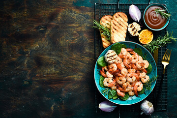 A plate of grilled shrimp with herbs, garlic and lemon. On a dark stone background. Top view.