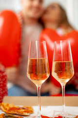 Two glass glasses of wine on background of defocused pair of lovers and red hearts. Valentine's Day holiday. Enjoying life.Love relationship in couple.