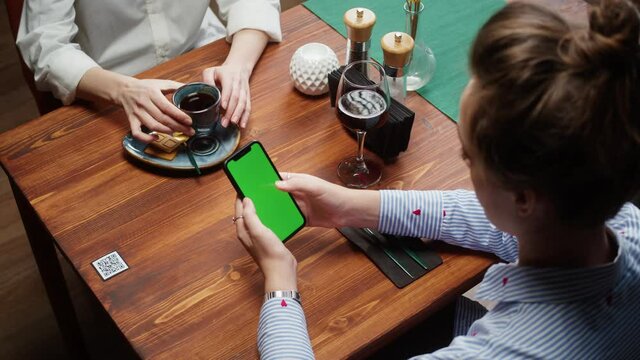 Woman using smartphone with chroma green screen, online menu in cafe. Scanning QR code in restaurant. Modern technology, ordering meal in application. Contactless touch-free payment in app.