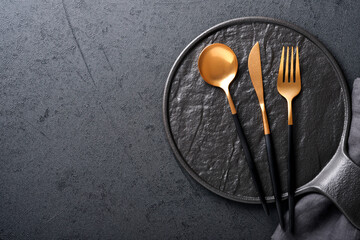 Gold spoon, fork, knife and clean empty black plate. Set of stylish black and gold cutlery on black...