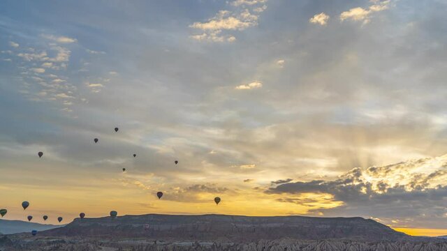 Many hot air balloons flying in air overhead in scenic golden morning sunrise cloudy sky with magic sun rays transparenting through white peaceful clouds. 4k stock video time lapse