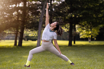 Young female practising yoga in public park at sunrise