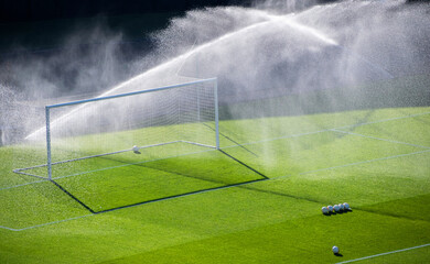 Sprinklers watering the grass by a goal on a football pitch