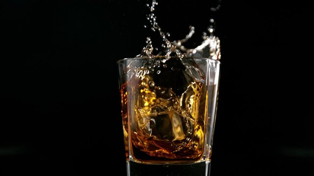 Super slow motion of falling ice cube into glass of whiskey or rum with camera motion. Filmed on high speed cinema camera, 1000 fps.