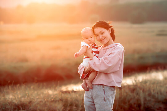 Portrait of a smiling woman standing in a field holding her baby boy, Sakon Nakhon, Isan, Thailand