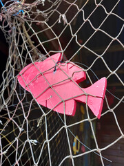 Decorative pink wooden fish hanging on fishing net. Rustic and vintage sea life decor. Fishing net with ornamental fish.
