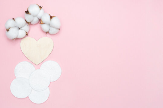 Cotton pads and wooden heart. Cosmetic pad and cotton flowers. Pink pastel background. Place for text. Copy space. Flat lay. Beauty and hygiene