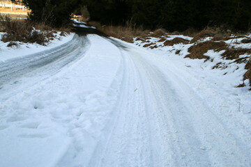 The detail of the narrow road in winter with risky driving conditions on snow and ice or black ice hiding in the shadows. 