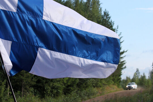 The detail of the Finnish flag waving in the wind taken during the Rally Finland. The racing car is in the background. 