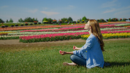 Young woman meditating on green grass. Hipster girl sitting in lotos outdoors. - obrazy, fototapety, plakaty