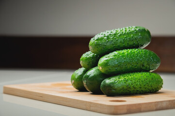 Close-up of several fresh cucumbers lie on a wooden cutting board on a white table. copy space vegetarian food