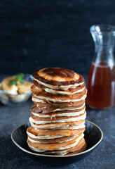 Pancakes with maple syrup, bananas stacked on top of each other on black plate