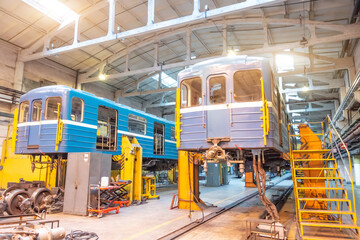 Subway cars and locomotives on jacks are raised for repair and replacement of wheeled bogies in the depot hangar.