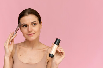 A beautiful smiling model applies foundation from a glass tube. Applying makeup to the face, smoothing the skin
