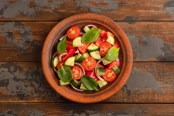 Vegetable salad with tomatoes, sweet pepper, spinach, red onion, cucumber top view, wooden background