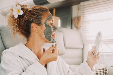 Young adult woman appliying cream beauty skin treatment mask on face using a mirror. Camper van lifestyle and healthy care female people activity. Pretty lady caring herself for aging