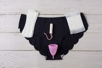 Different types of feminine menstrual hygiene materials products such as pads cloths tampons and cups with underpants. White wooden background - obrazy, fototapety, plakaty
