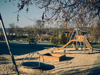 Fototapeta premium The morning, autumn sun illuminates the playground, there is a small carousel, swings and slides, there is no one, autumn mood