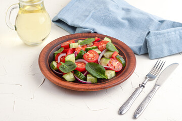 Vegetable salad with tomatoes, sweet peppers, spinach, red onion, cucumber on a white concrete background