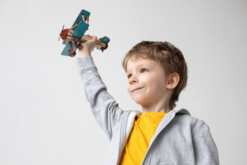 Smiling dreamy boy with a wooden plane in his hands imagines, on a white background. Happiness and freedom