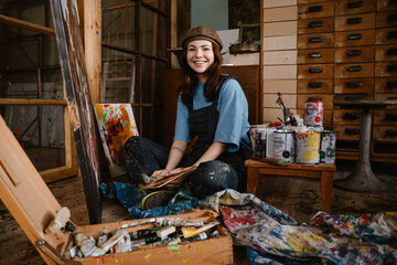 Young woman wearing overall painting on canvas while sitting on floor