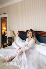 Fototapeta na wymiar Bride morning. Girl in a white peignoir on the bed. Preparing the bride for the upcoming wedding.