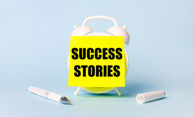 On a light blue background - a white handle and an alarm clock with a bright yellow sticker glued to it with the text SUCCESS STORIES