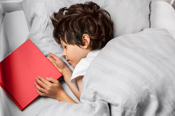 Boy sleeping at night in his bed with a red book