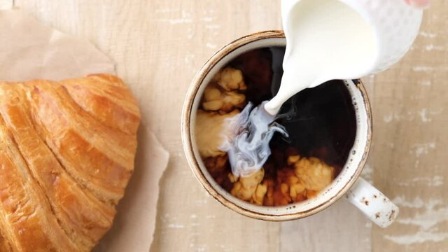 Slow motion pouring cream milk in black coffee. Top view. Coffee with croissant