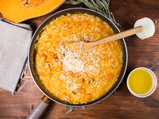 Cooking risotto with pumpkin - ready risotto with grated cheese in a frying pan on the table with ingredients, top view