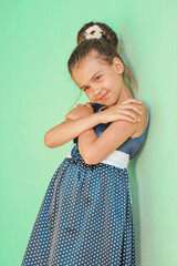 a young brunette girl in a blue polka dot dress stands against the wall in the summer
