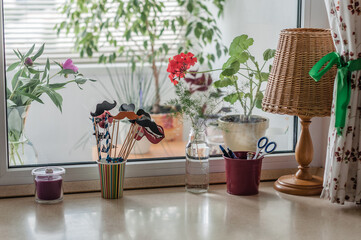 Work area at home, a window-sill, a lot of plants, a lamp with a shade and curtains in a flower.