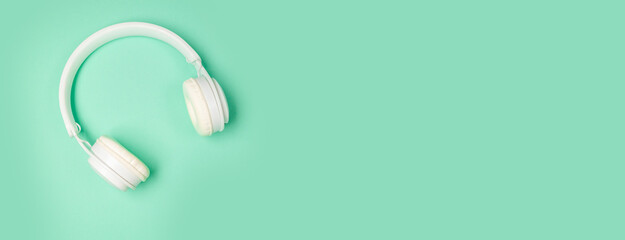 Studio shot of modern white wireless headphones isolated on green mint background. Music or podcast...