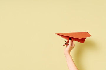 A woman's hand holds terracotta paper airplane on olive green background