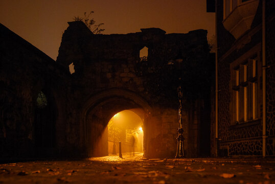 Illuminated cobbled street in an old town with light reflections on cobblestones, archway with ghostly figure