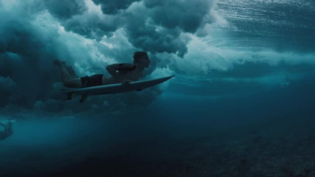 Surfing in Maldives. Teen boy dives with surf board underwater to pass the ocean wave