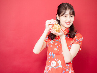 Asian young woman wearing traditional cheongsam qipao dress showing Gold ingot for celebrating chinese new year on red background.