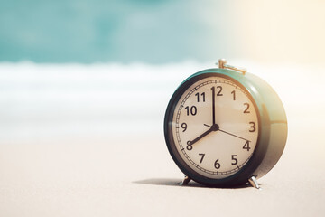 Clock on sand beach in morning suns light with smooth wave background. Copy space of time and summer holiday concept.