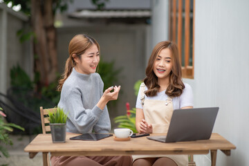 Two Asian young women working on laptop while sitting in a cafe.